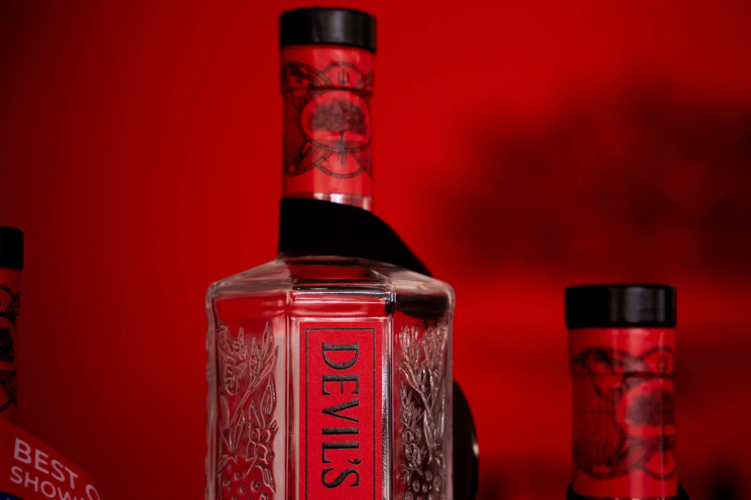 Devil's Grin Texas Gin bottle with embossed botanical design against a red background