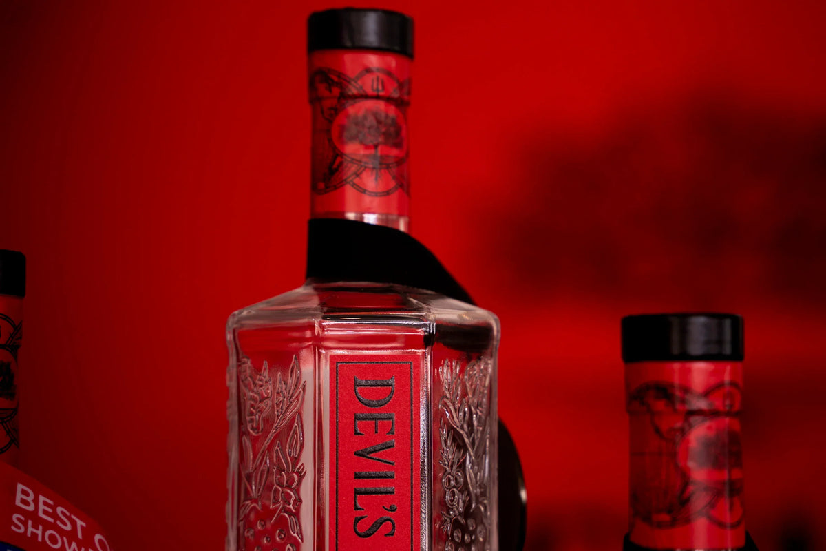 Devil's Grin Texas Gin bottle with embossed botanical design against a red background