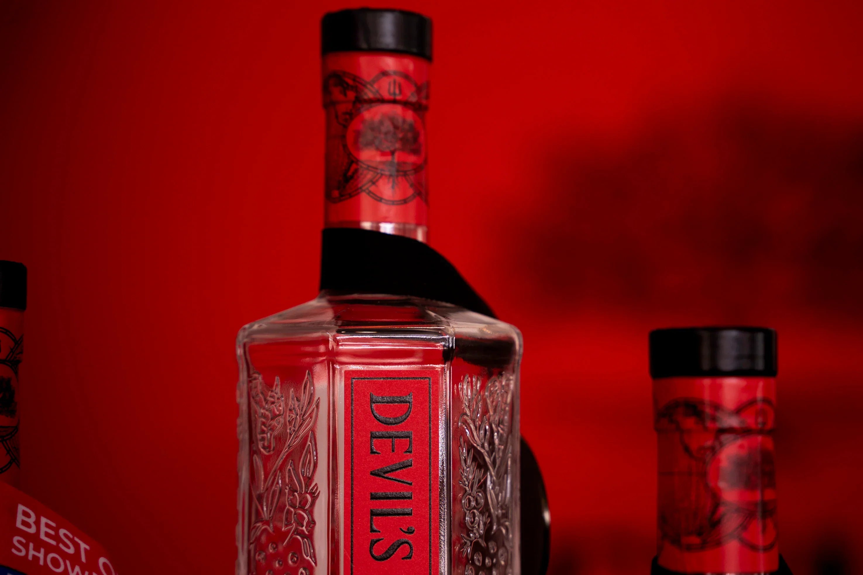 Devil's Grin Texas Gin bottle with embossed botanical design against a red background