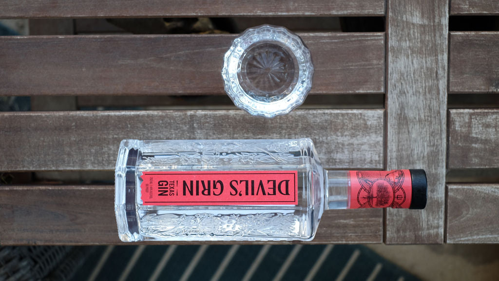 Overhead view of Devil's Grin Texas Gin bottle and a glass of vodka on a weathered wooden slatted table