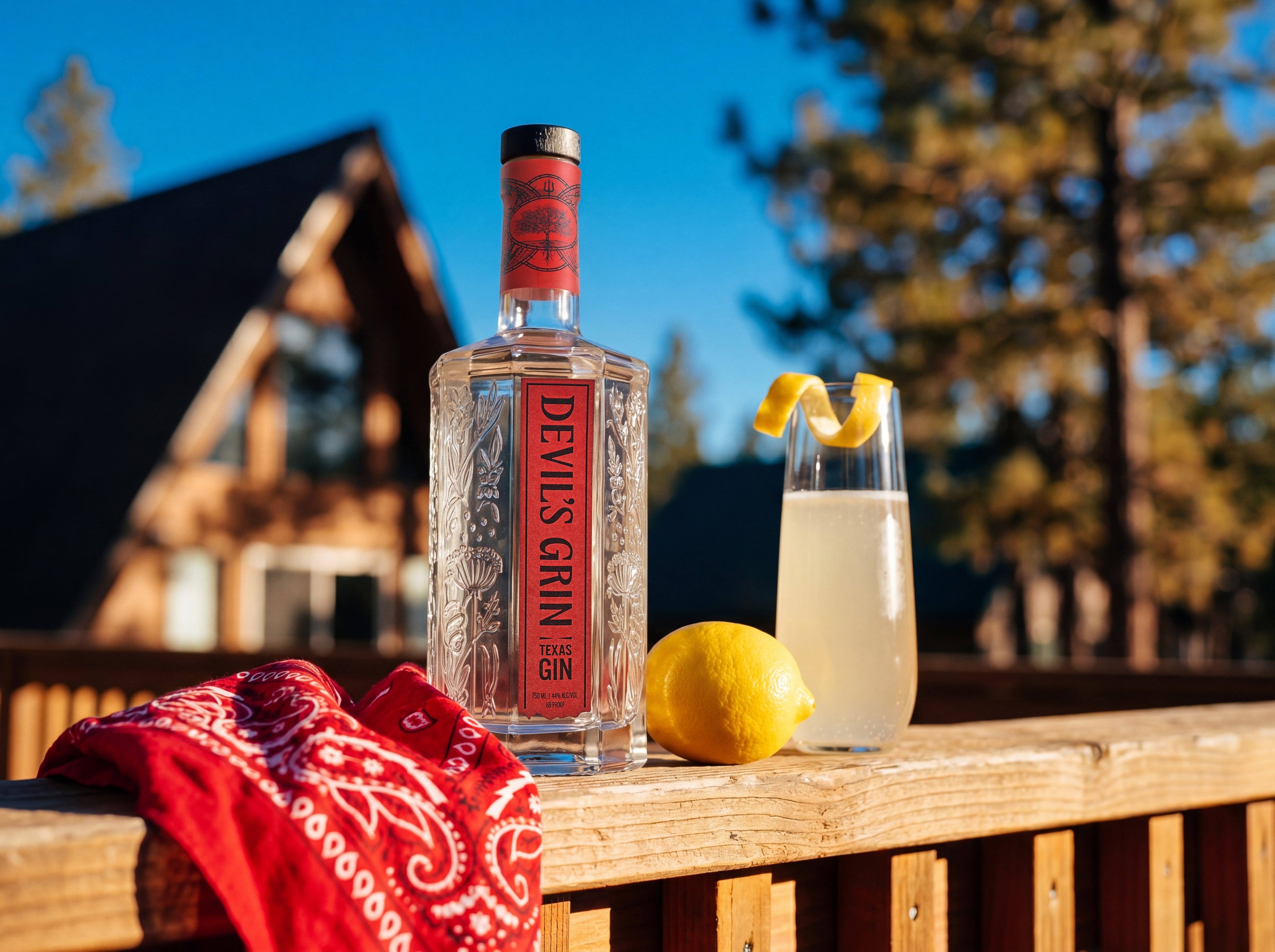 Devil's Grin Texas Gin bottle with a French 75 cocktail and fresh lemon on a cabin deck