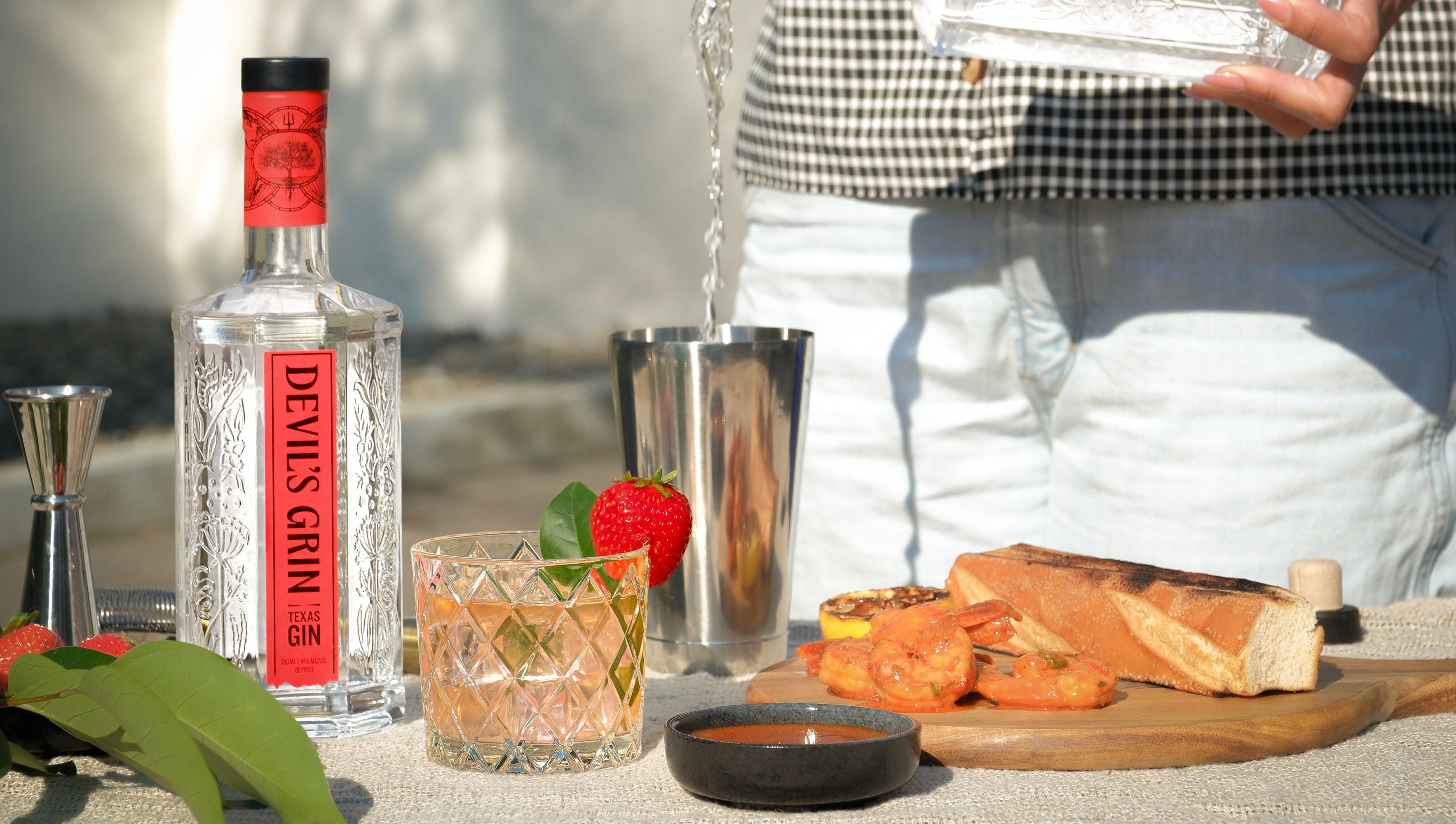 Devil's Grin Texas Gin bottle with a strawberry-garnished gin punch in a crystal rocks glass