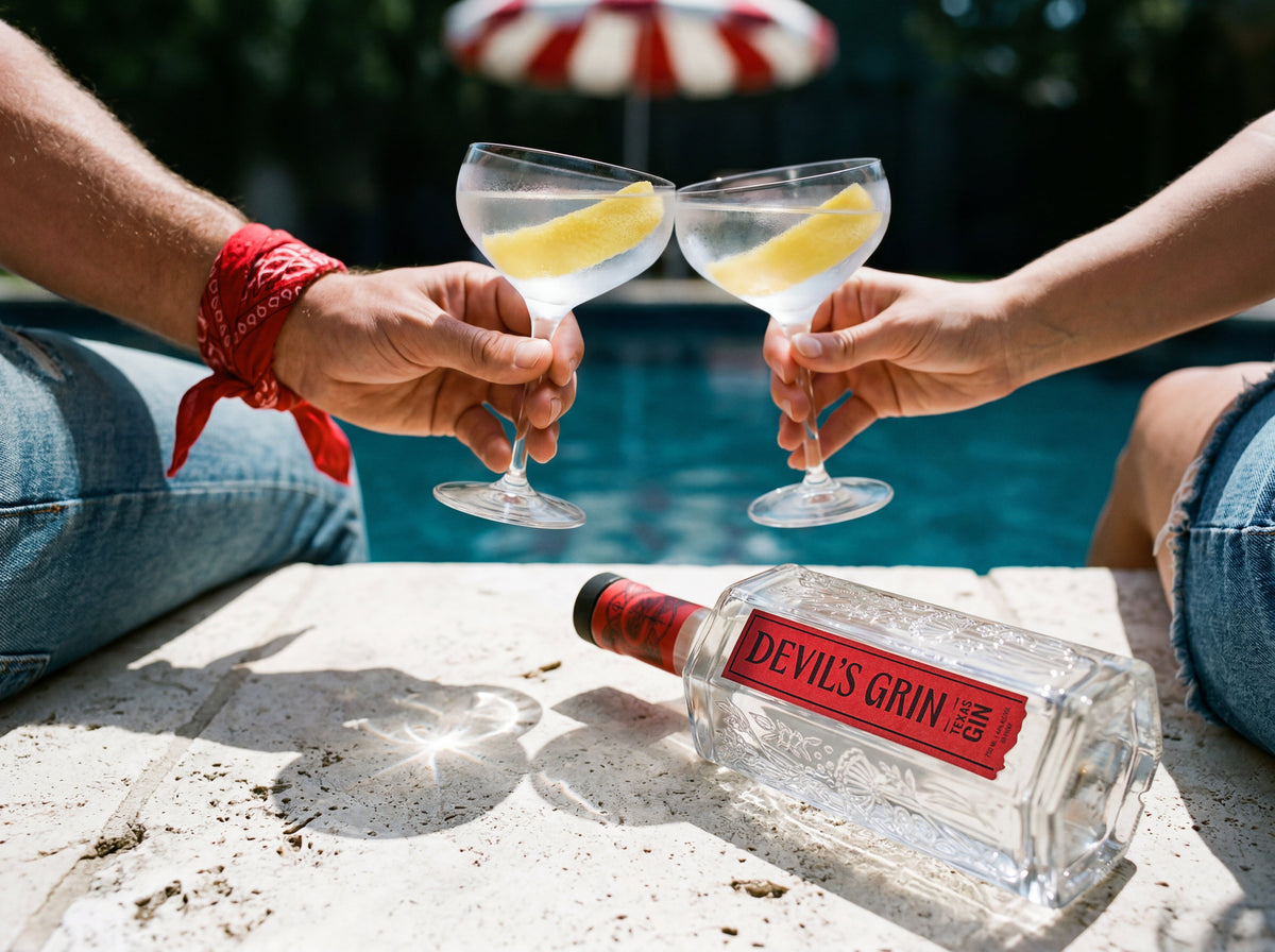 Two people toasting with lemon-garnished gin martinis poolside with a bottle of Devil's Grin Texas Gin