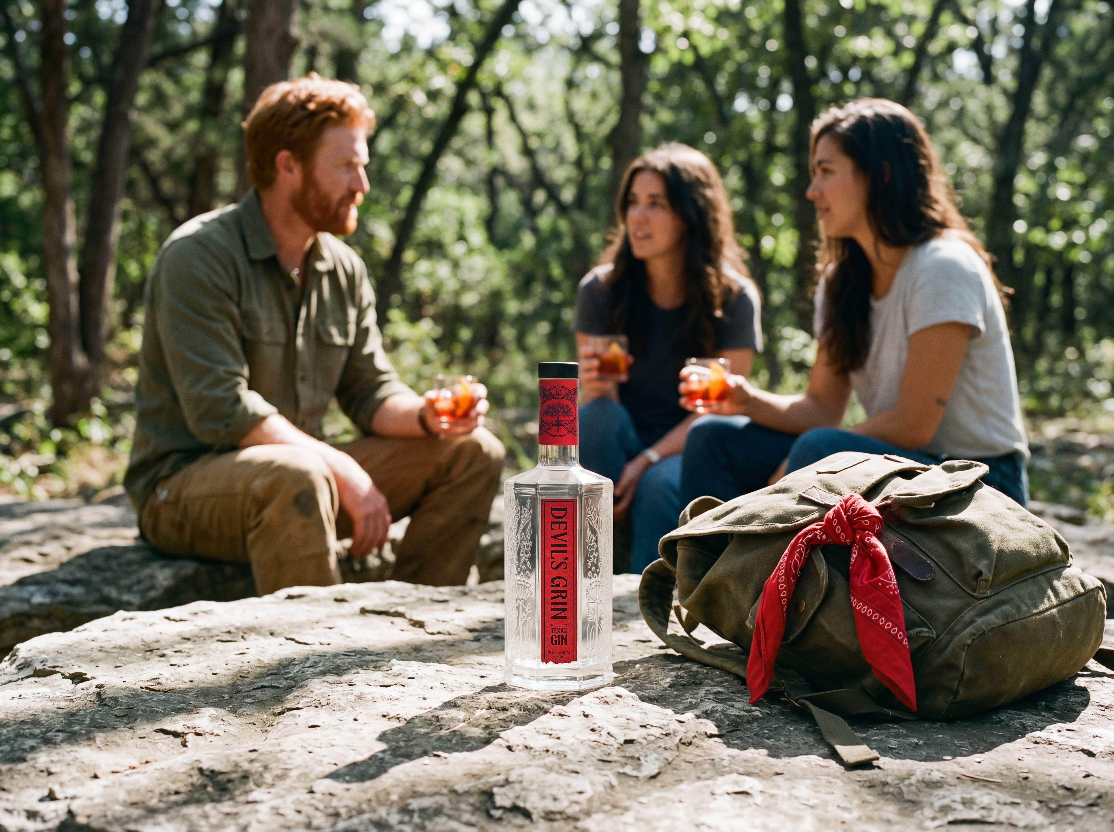 Devil's Grin Texas Gin bottle on a rock with friends enjoying negroni cocktails on a forest hike