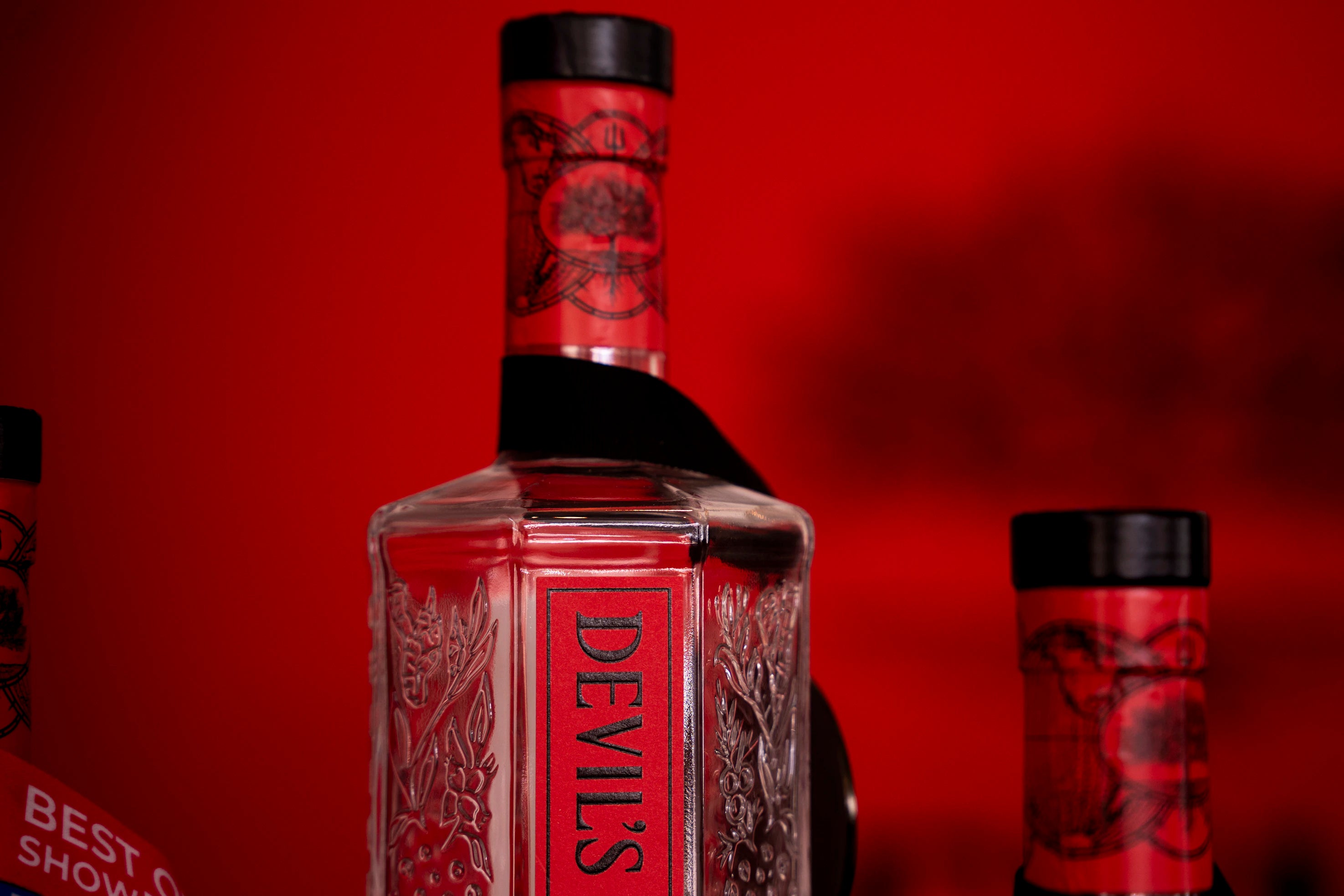 Devil's Grin Texas Gin bottle with embossed botanical design against a red background