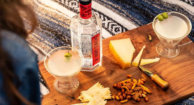 Devil&rsquo;s Grin bottle and two coupes on a cheese board