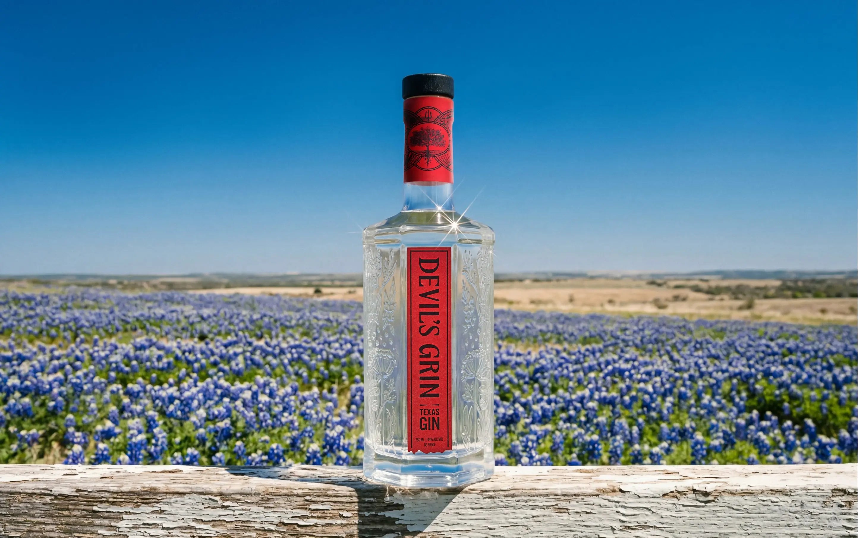 Devil&rsquo;s Grin bottle on a weathered rail in a Texas bluebonnet field