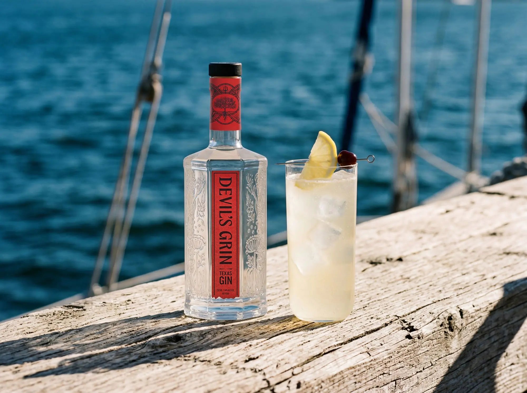 Devil&rsquo;s Grin bottle and a highball on a dock by the water